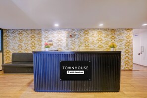 A reception desk labeled 'TOWNHOUSE' with a 'YO-Serviced' sign, a grey sofa, and patterned wallpaper. - Townhouse APMC Metro Station  (Ahmedabad)