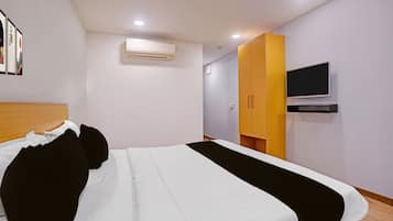 Una habitación de hotel con una cama, un televisor, un equipo de aire acondicionado y un armario de madera.