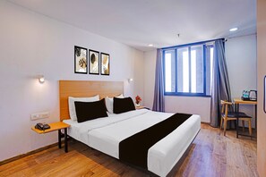 A hotel room with a bed, bedside table, lamp, and a window with curtains. - Townhouse APMC Metro Station  (Ahmedabad)