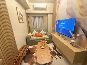 Ein modernes Wohnzimmer mit einer Couch, einem Couchtisch mit einer Vase, einer Klimaanlage und einem Flachbildfernseher, der ein Social-Media-Profil anzeigt.