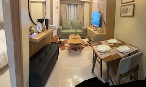 A compact hotel room with a sofa, a small dining table set for two, a television, and a desk with a computer. - Cozy condo unit at the heart of Metro Manila, Near Mall of Asia and Airports (Pasay City)