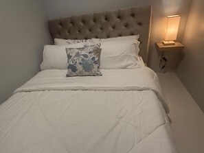 Ein ordentlich bezogenes Bett mit einer gesteppten Decke und zwei Kissen, eines davon mit Blumenmuster.
