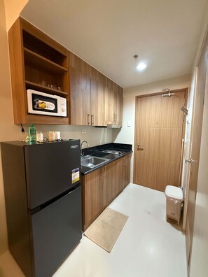 Eine kleine Küche mit Holzausstattung, einem schwarzen Kühlschrank, einer Spüle und einem Mülleimer.