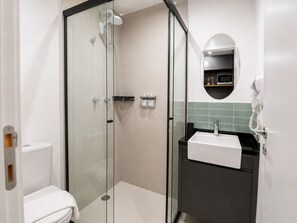 A modern bathroom with a glass-enclosed shower, a white toilet, a black sink with a mirror above it, and a hairdryer mounted on the wall. - Nik Paulista 513 (Vila Mariana)