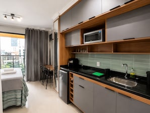 A compact kitchen with a microwave, sink, and a dining area with a table and chairs. - Nik Paulista 513 (Vila Mariana)