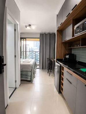 A modern kitchen with a built-in microwave, a coffee machine, and a small dining area with a table and chairs. - Nik Paulista 513 (Vila Mariana)