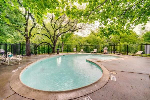 Ein Pool mit geschwungener Kante, umgeben von einem schwarzen Metallzaun und Bäumen.