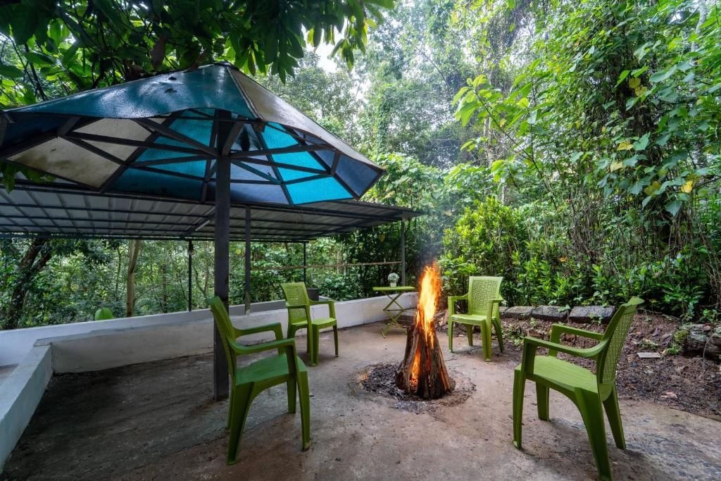 Un área de estar al aire libre con un brasero, sillas verdes y una sombrilla.