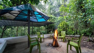 Un área de estar al aire libre con un brasero, sillas verdes y una sombrilla.