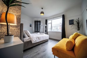Ein modernes Hotelzimmer mit einem Bett, einem gelben Sessel, einer Topfpflanze, einer Lampe und einem Fenster mit Blick.