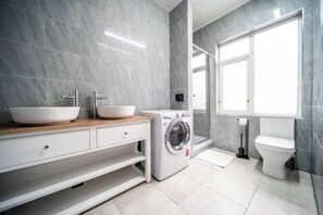 Ein modernes Badezimmer mit einem Doppelwaschbecken, einer Waschmaschine und einer Toilette.