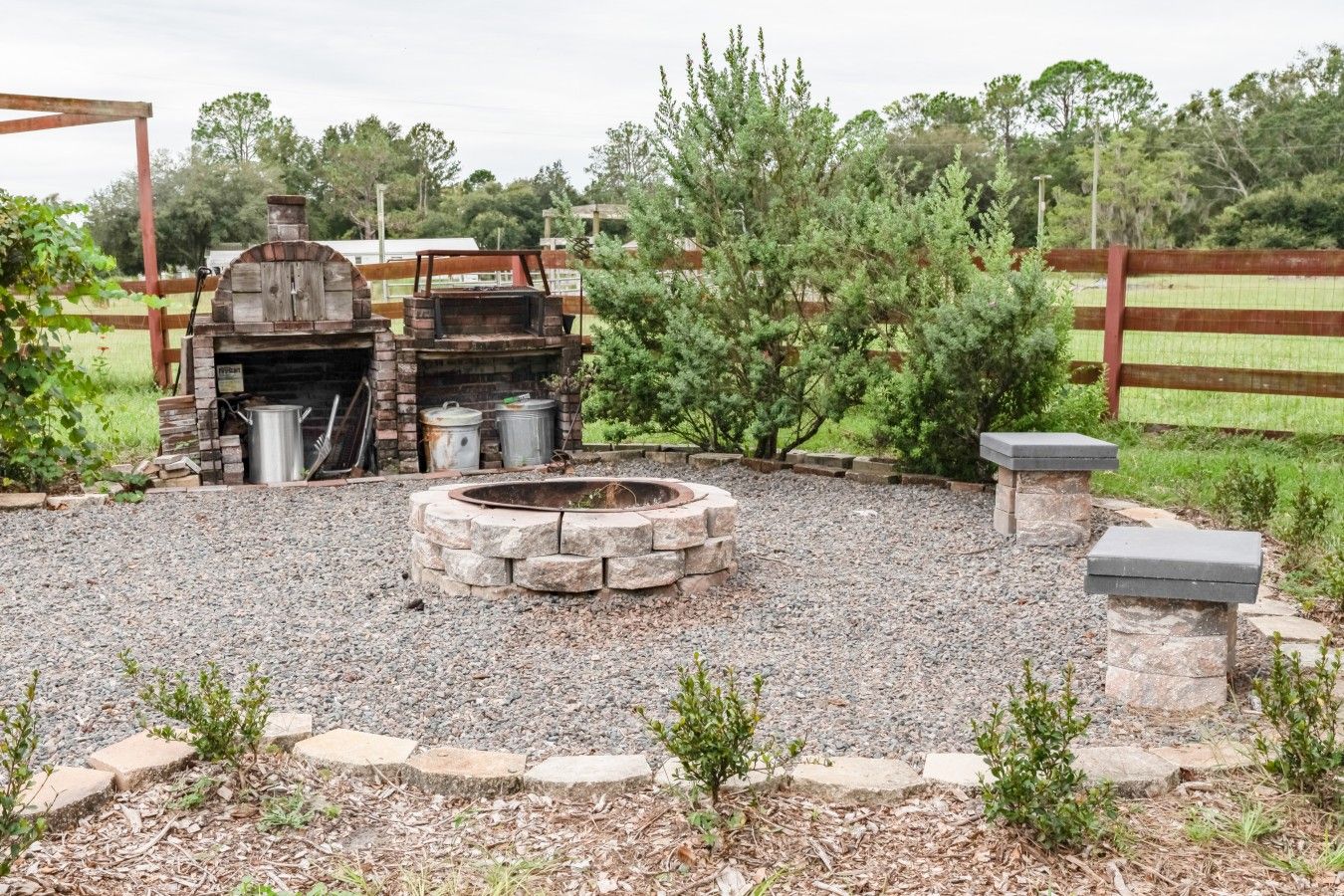An outdoor barbecue area with a stone fire pit, a grill, and a metal water container.