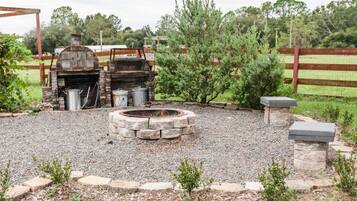 An outdoor barbecue area with a stone fire pit, a grill, and a metal water container.