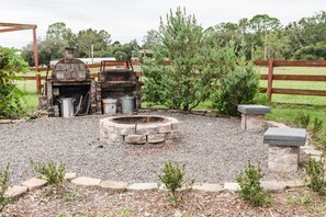 An outdoor barbecue area with a stone fire pit, a grill, and a metal water container. - defaultName (Land O` Lakes)