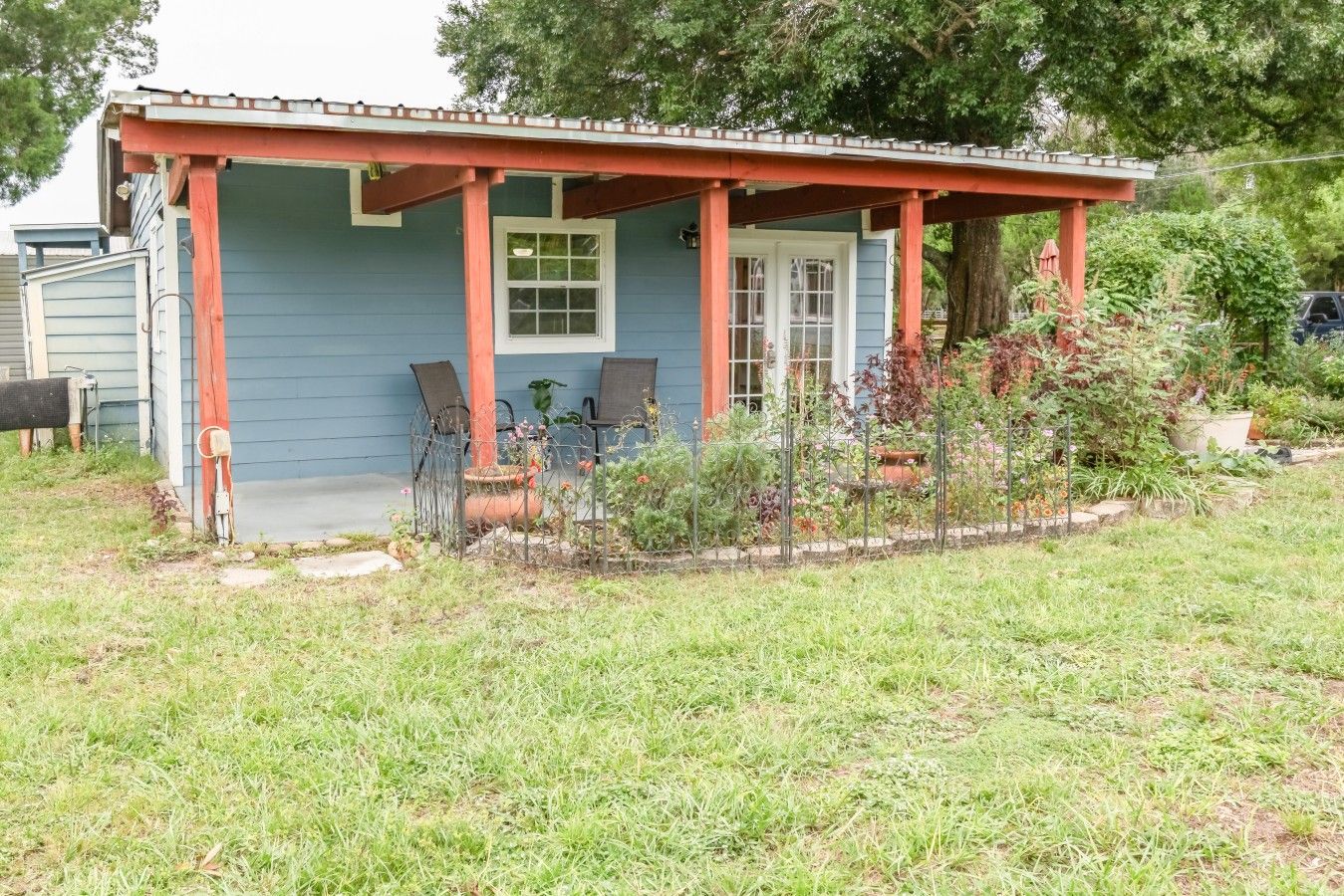 Une maison avec un porche, deux chaises, une plante en pot et une boîte aux lettres.