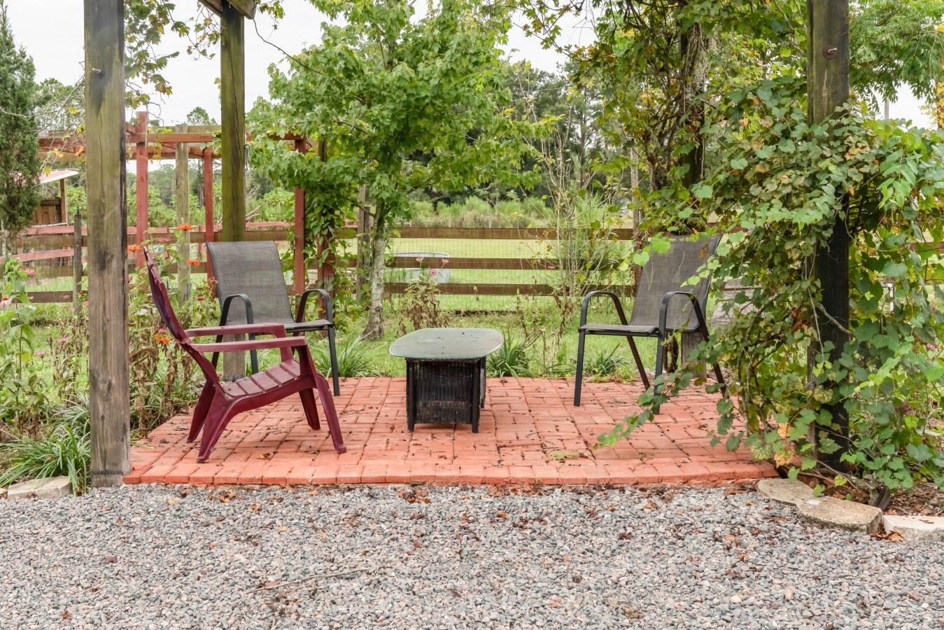 Un espace extérieur aménagé avec deux chaises et une table, entouré d’une pergola en bois et de verdure.