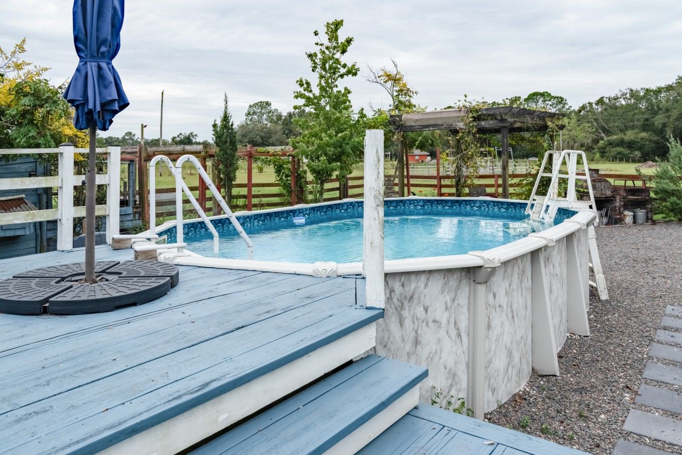 Een bovengronds zwembad met treden, omringd door een houten terras en een pergola.