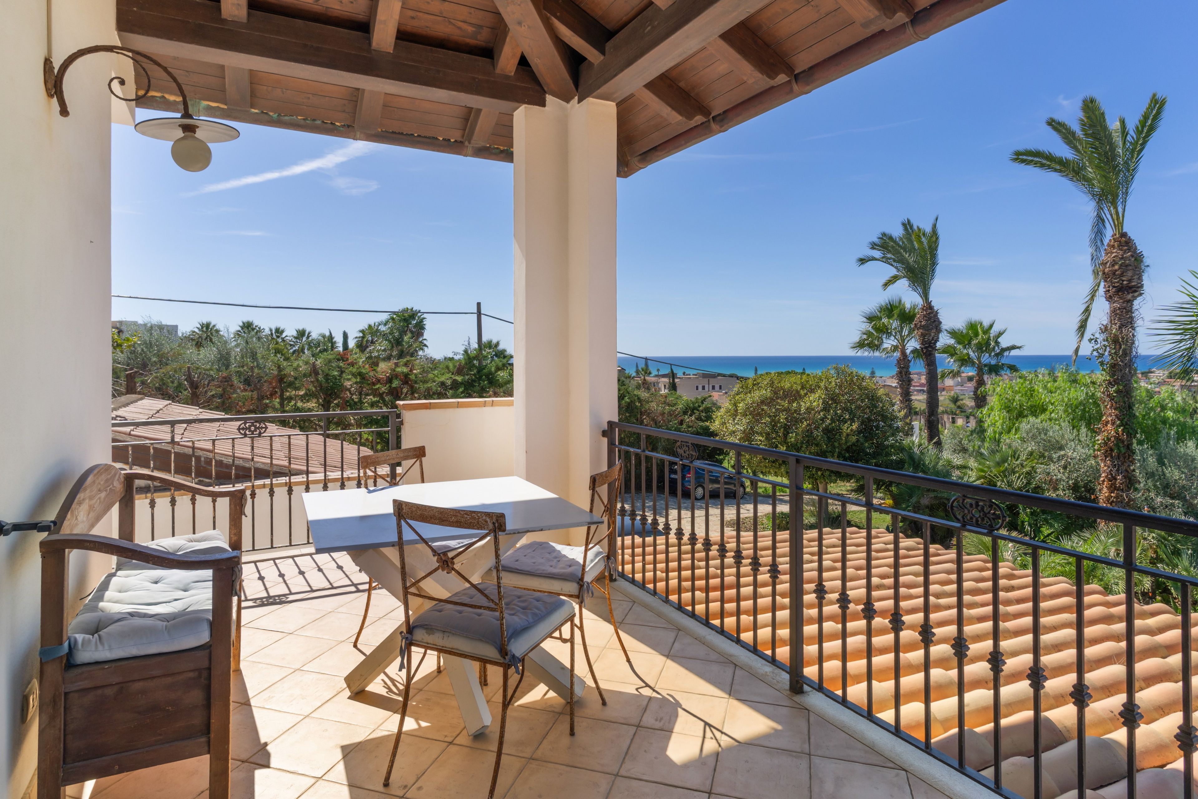 A balcony with a table and chairs, a view of the sea, and a palm tree.