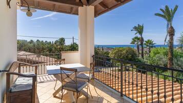 A balcony with a table and chairs, a view of the sea, and a palm tree.