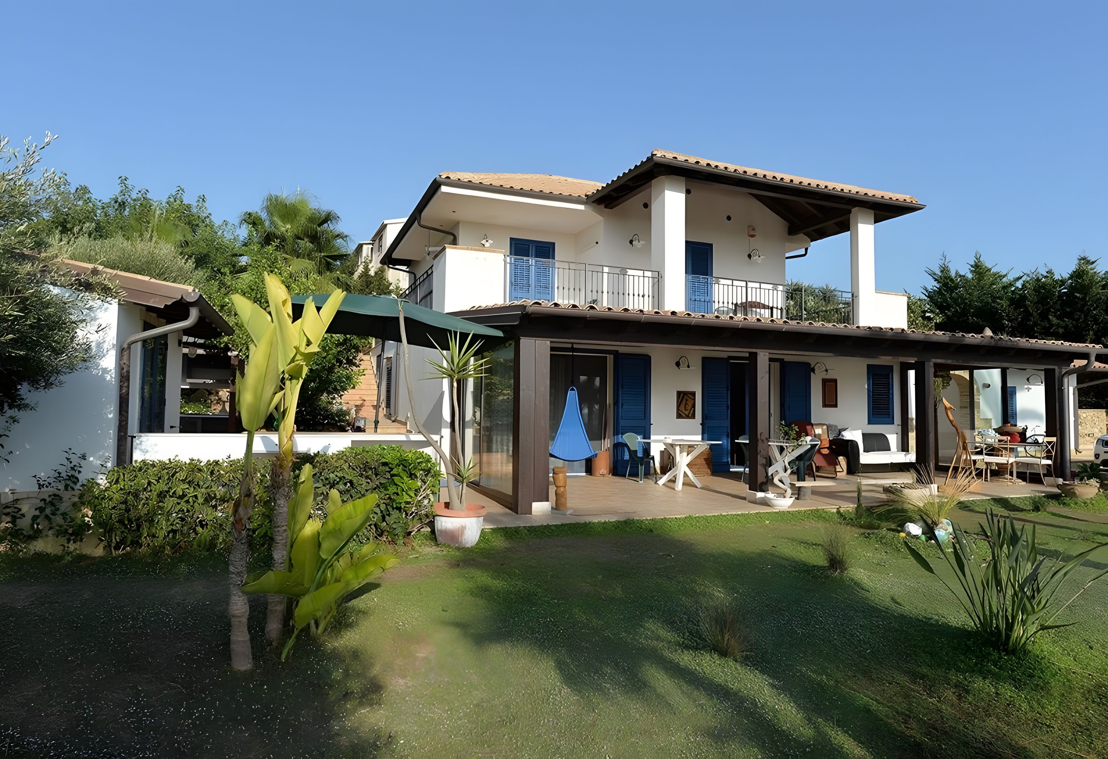 Een huis met twee verdiepingen, een balkon, een overdekt terras en een verzorgde tuin.