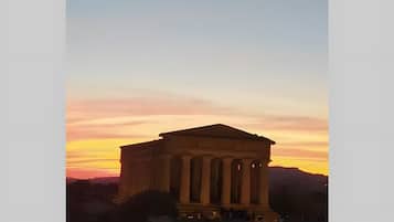 Un bâtiment classique, orné de colonnes, qui ressemble probablement à un monument historique, se dressant sur fond de ciel au coucher du soleil.