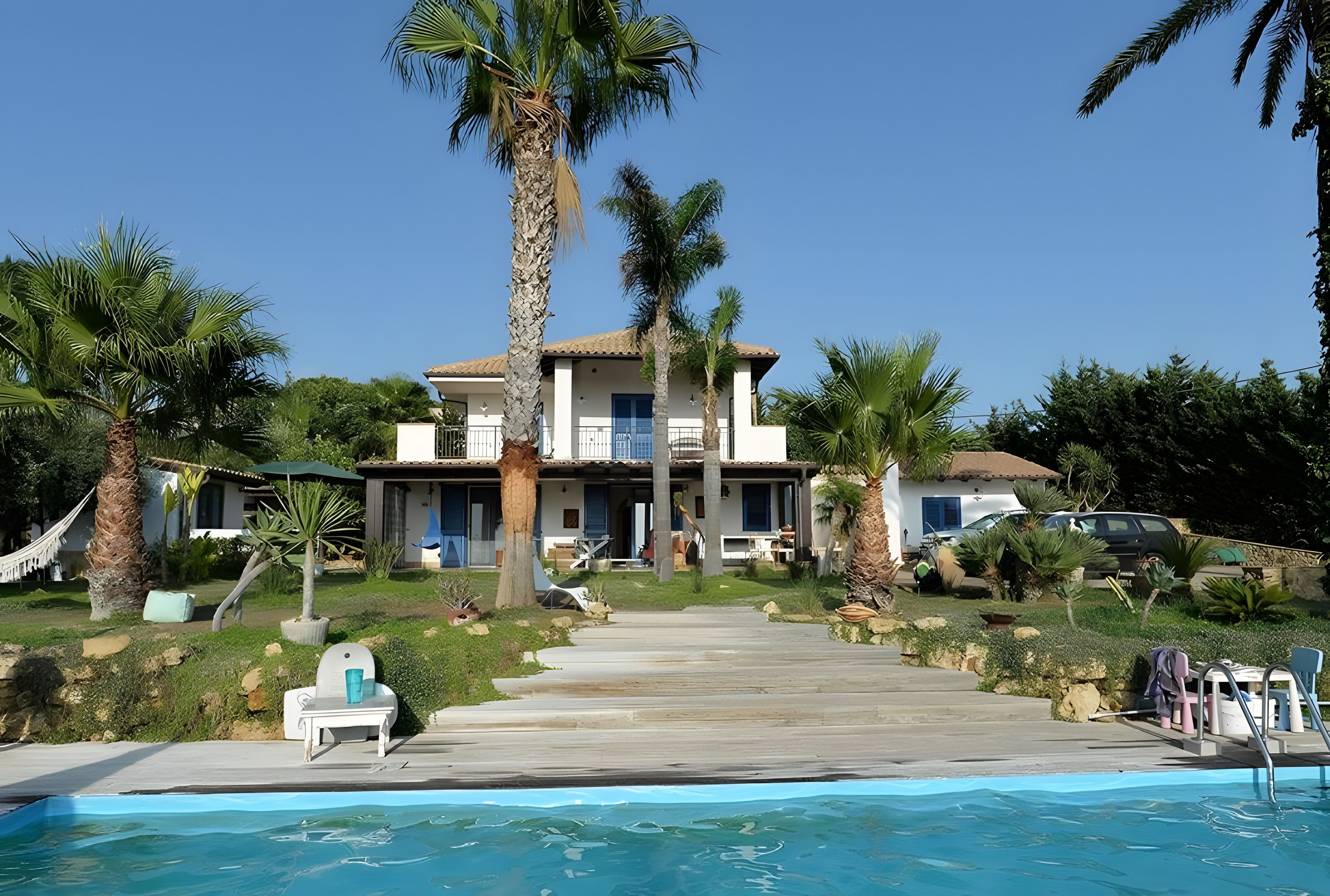 Een tweelaags huis met een zwembad, palmbomen en een heldere lucht.
