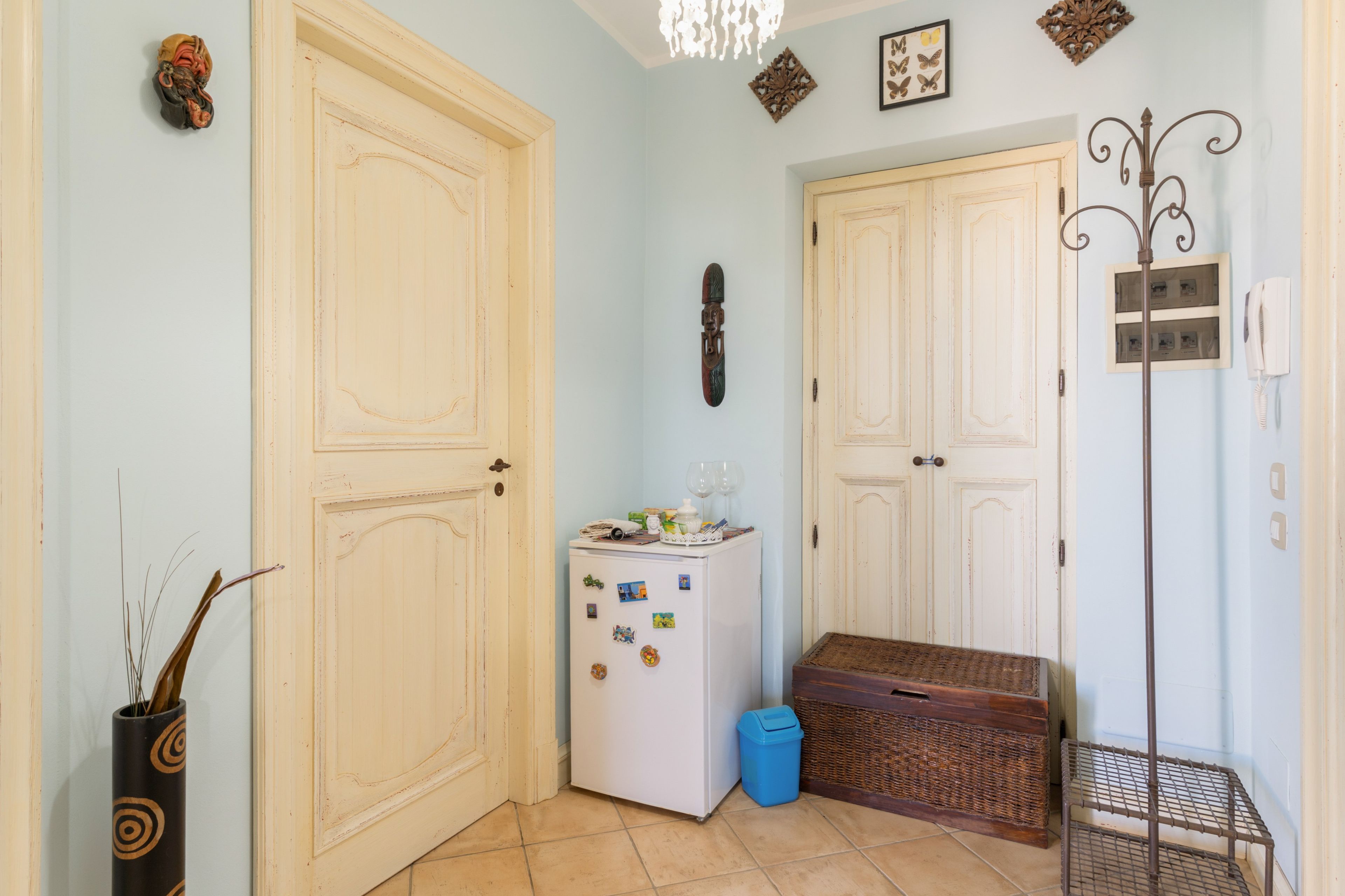 A hallway with two white doors, a refrigerator with magnets, a blue trash bin, and a wicker basket.