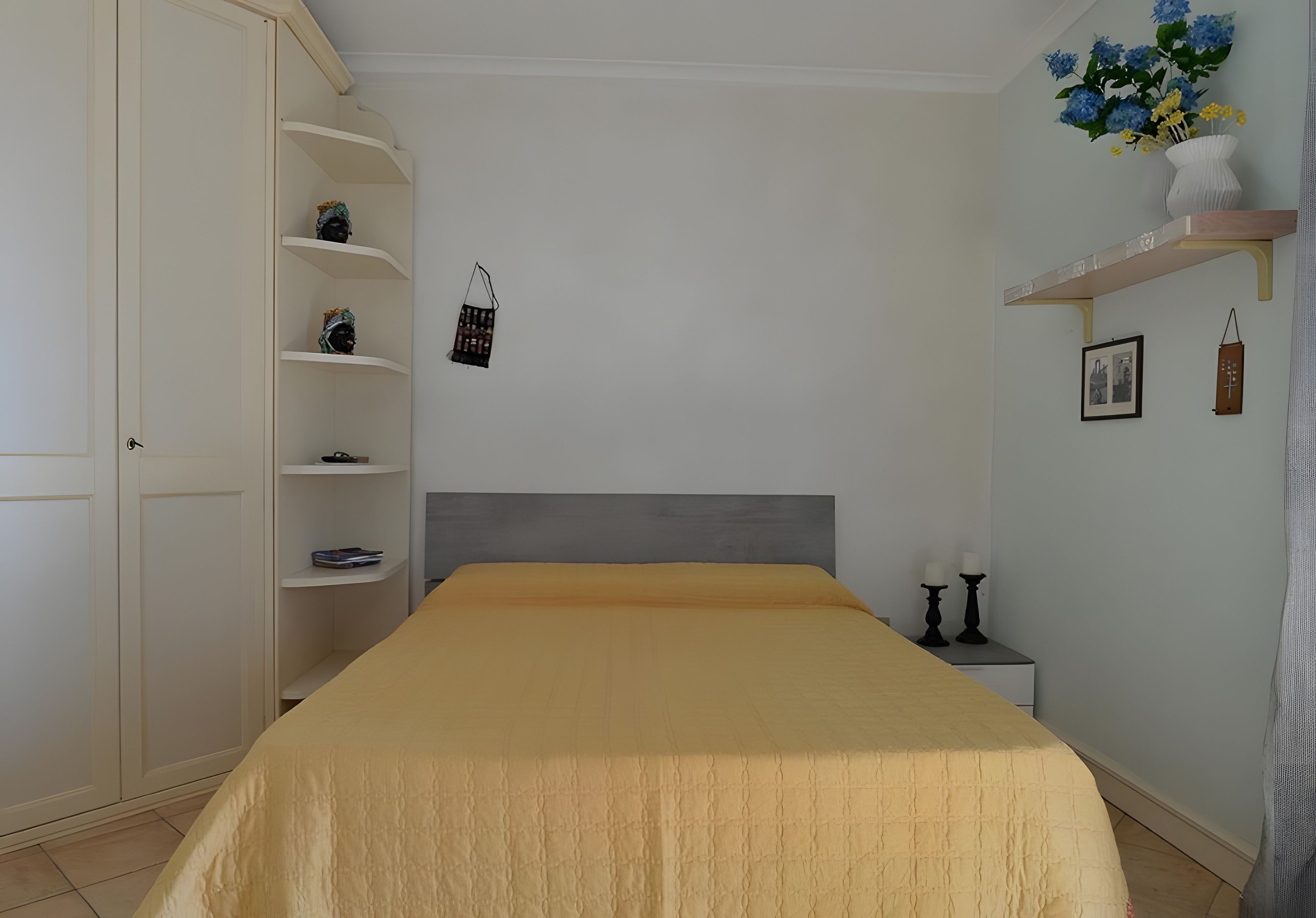 Een slaapkamer met een bed, een kledingkast, een nachtkastje en een wandplank met decoratieve objecten.