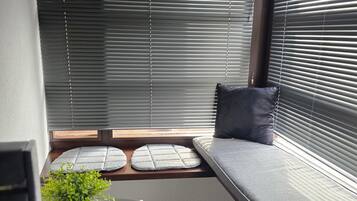 Un rincón con asientos, una ventana, una mesa pequeña con una planta y una revista.