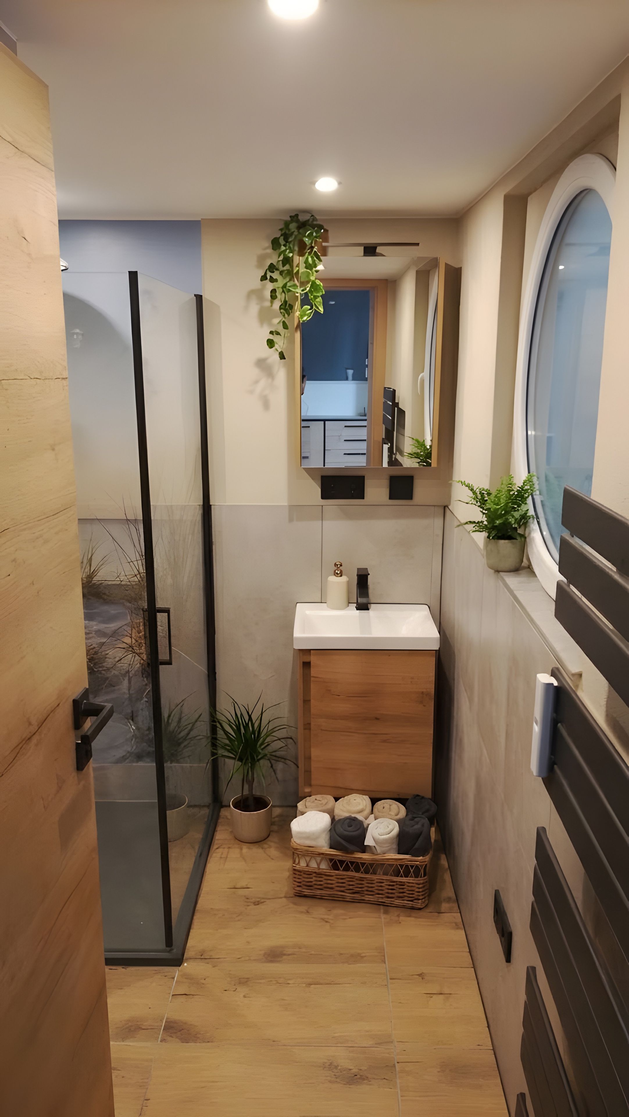 A compact bathroom with a glass shower enclosure, a sink with a mirror above, and a small window.