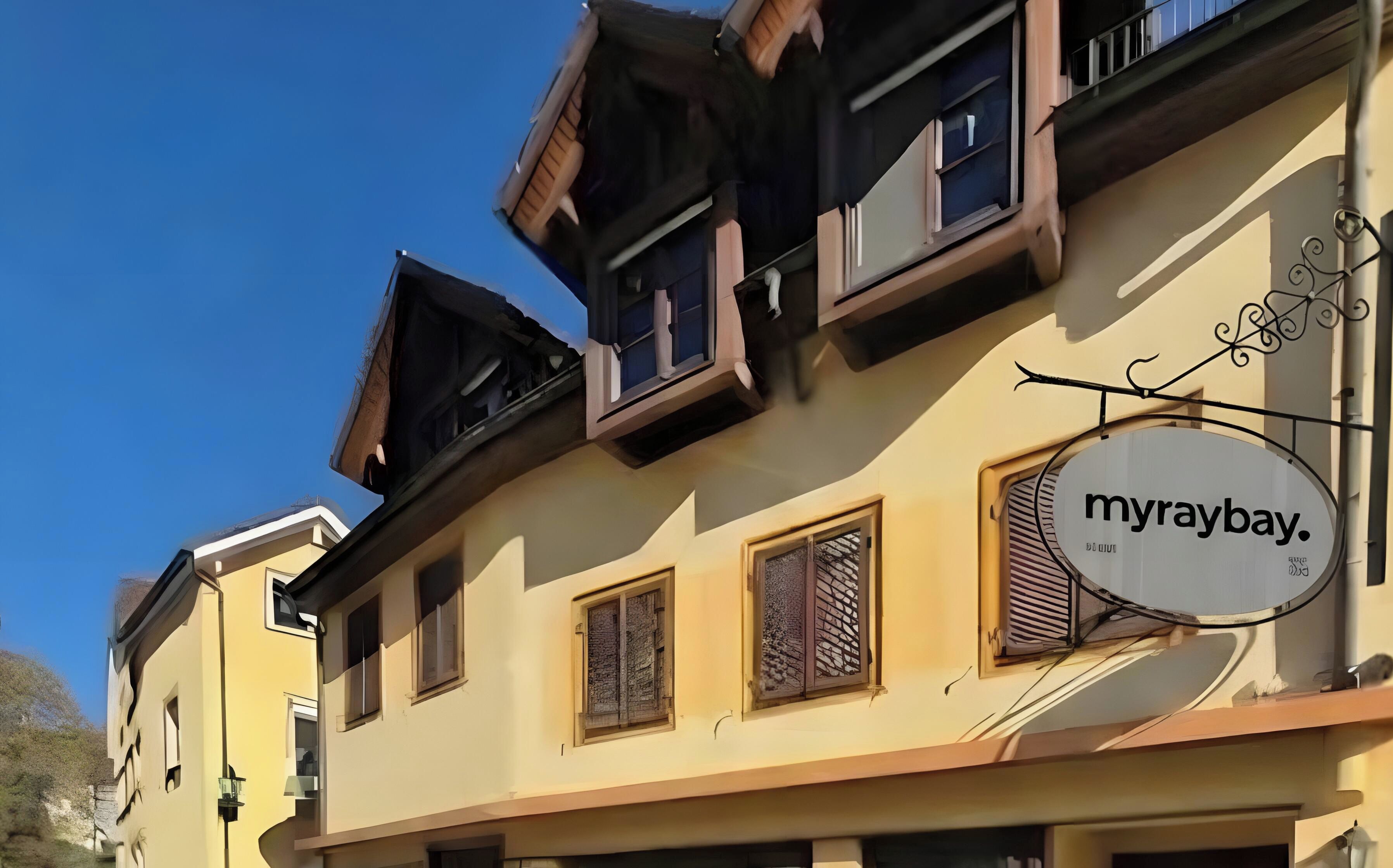 Ein Gebäude mit einem Schild mit der Aufschrift 'myraybay'. Es hat mehrere Fenster mit Fensterläden, eine Satellitenschüssel und ein dekoratives Metallschild.