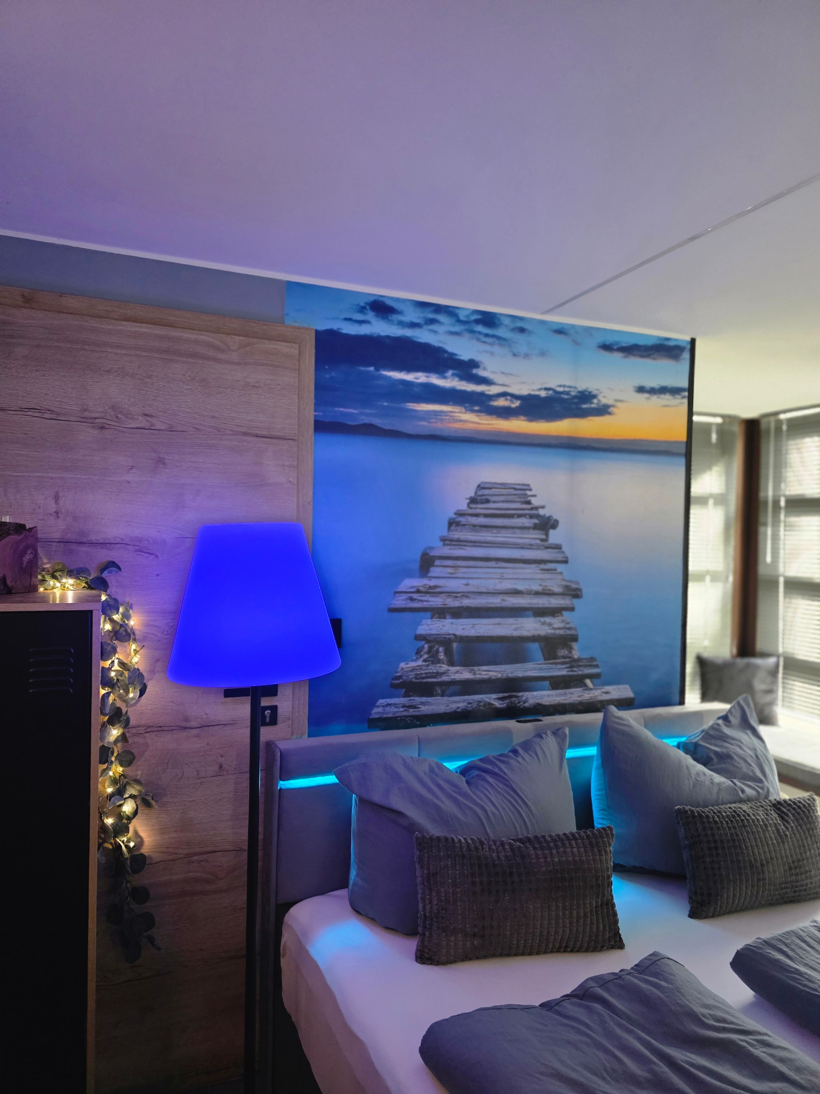 Ein Schlafzimmer mit einem Bett, einem Nachttisch, einer Lampe und einem Wandbild.