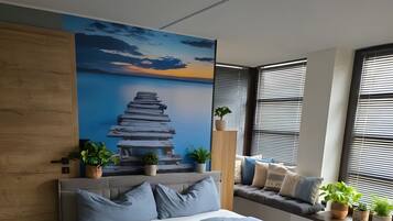 A modern bedroom with a large bed, a mural on the wall, and potted plants.