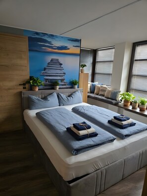 Een moderne slaapkamer met een groot bed, een muurschildering en potplanten.