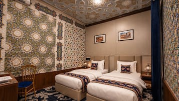 Habitación de hotel con dos camas, un escritorio, una silla y un papel tapiz estampado.