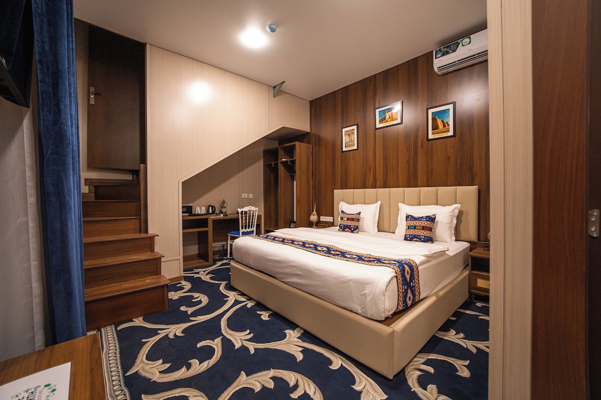 A hotel room with a large bed, a desk, and a chair. There is a staircase leading to another level.