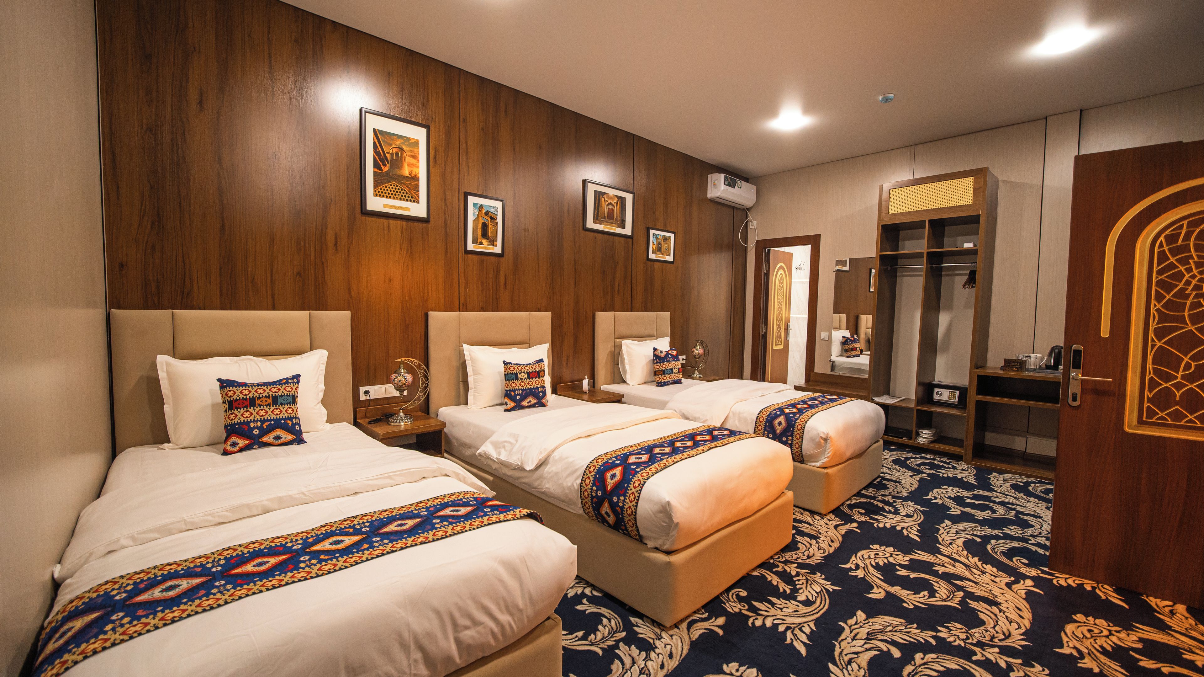 A hotel room with three beds, a wardrobe, a mirror, and a patterned carpet.