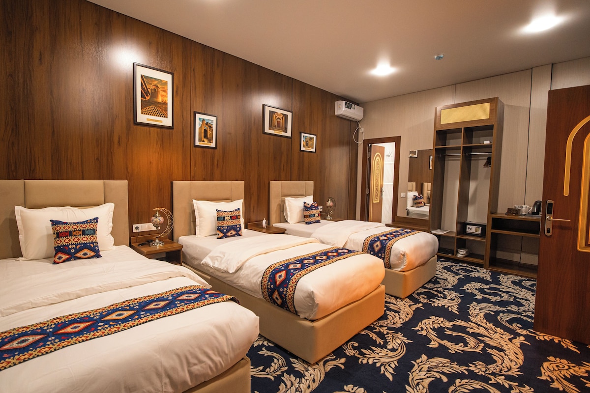 A hotel room with three beds, a wardrobe, a mirror, and a patterned carpet.