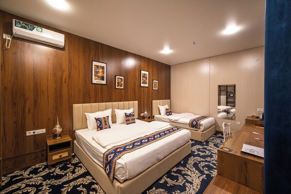 Habitación de hotel con dos camas, un escritorio, un espejo y aire acondicionado instalado en la pared.