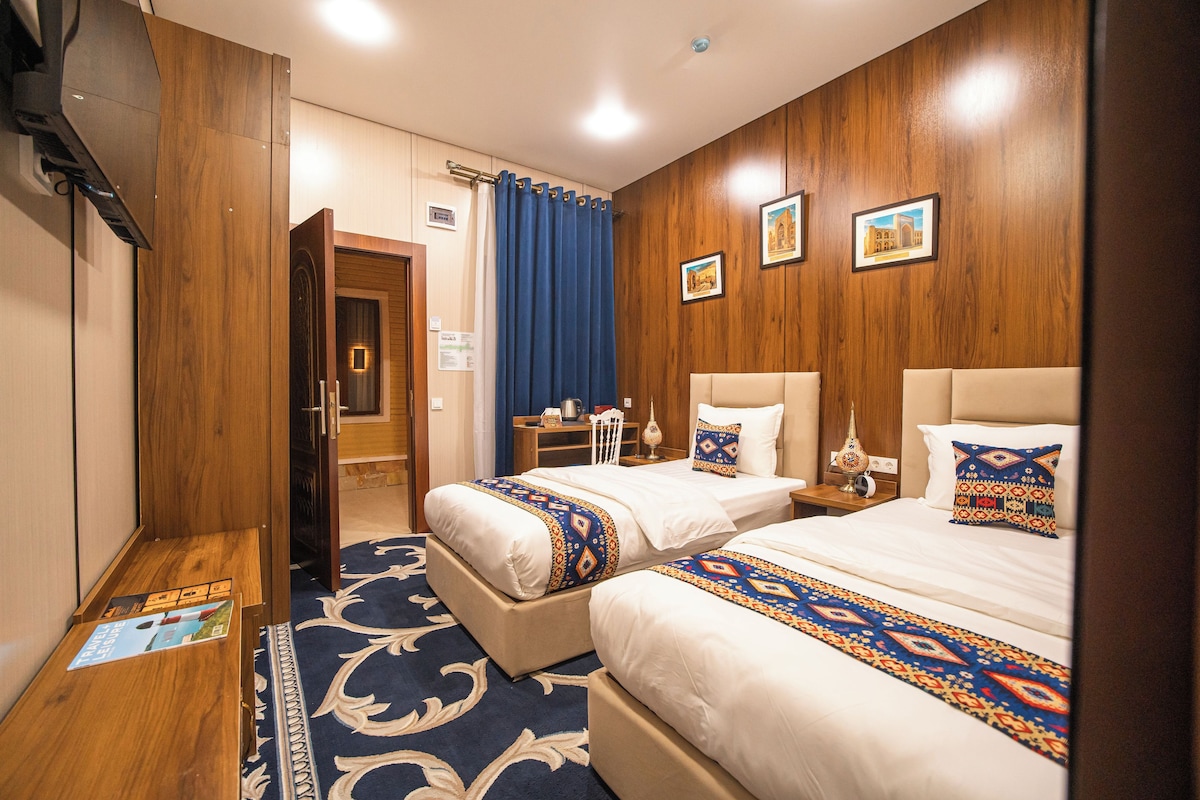A hotel room with two beds, a desk, a chair, a nightstand, and a wall-mounted TV.