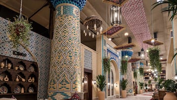 Un vestíbulo amplio con techos altos, columnas decorativas, plantas colgantes y baldosas con diseños tradicionales.