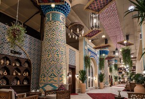 Un vestíbulo amplio con techos altos, columnas decorativas, plantas colgantes y baldosas con diseños tradicionales.