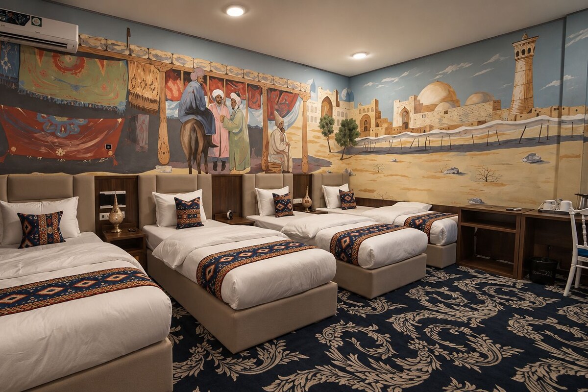 Habitación de hotel con tres camas, un escritorio y un mural que representa una escena desértica.