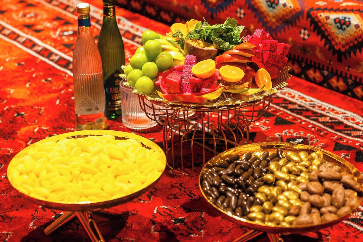 Una mesa de comedor con diversos alimentos y una botella, sobre una alfombra estampada.