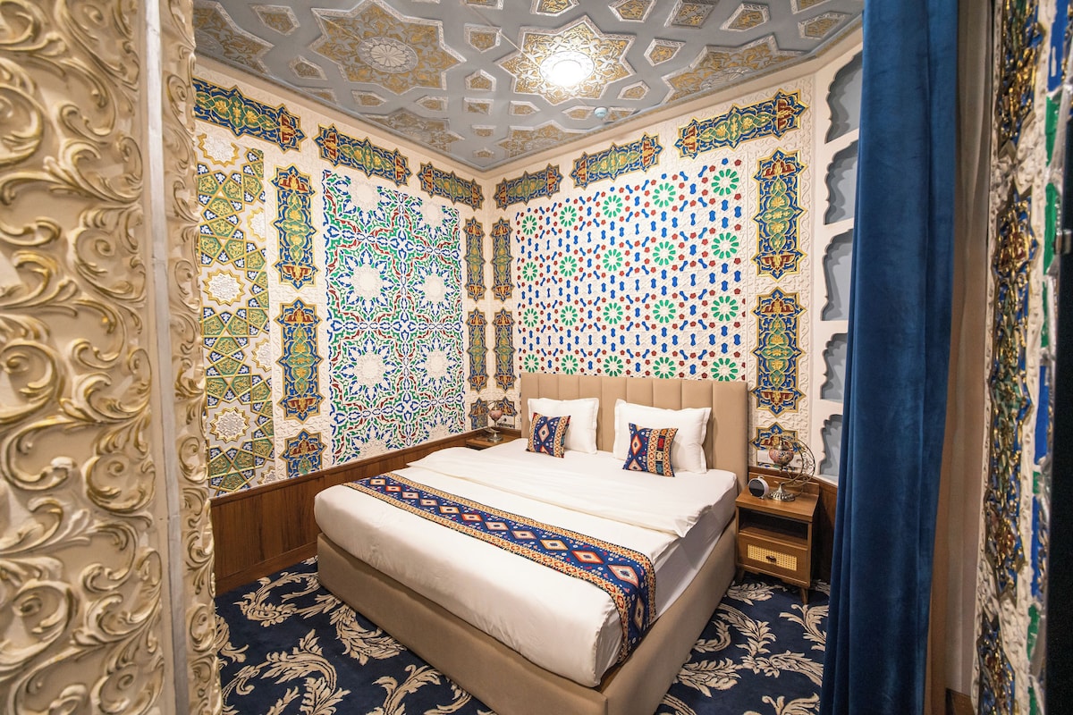 A room with a large bed, ornate wall patterns, and a decorative ceiling.