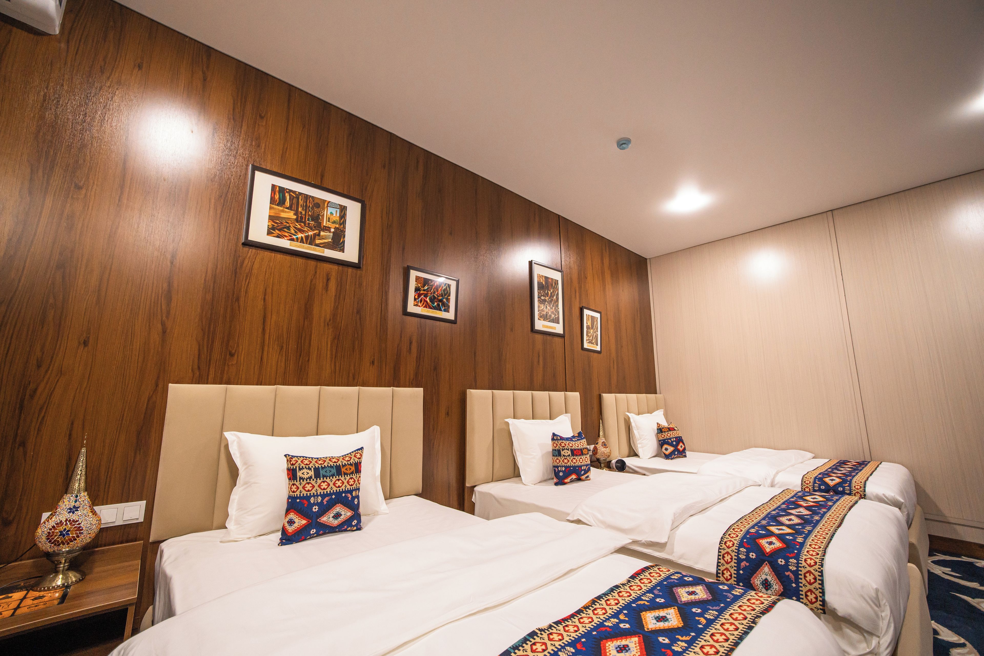 A hotel room with two beds, a wooden wall, and framed artwork.