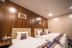 A hotel room with two beds, a wooden wall, and framed artwork. - Old Bazaar Boutique Hotel (Buxoro)
