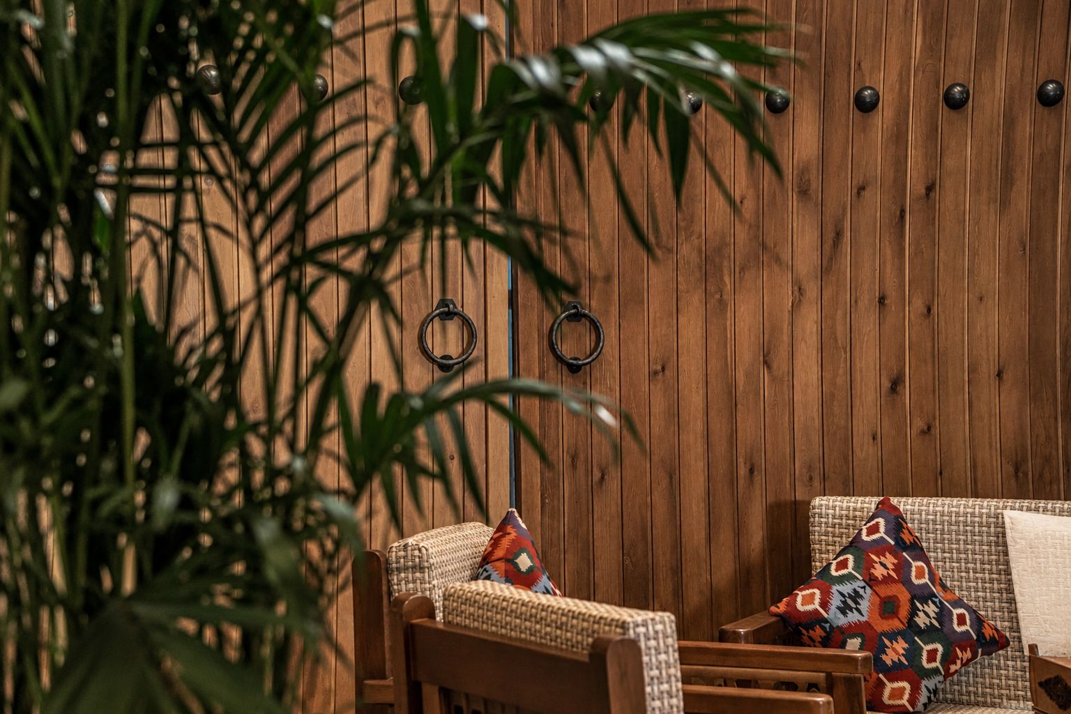A wooden wall with two rings and a woven chair with a patterned cushion.