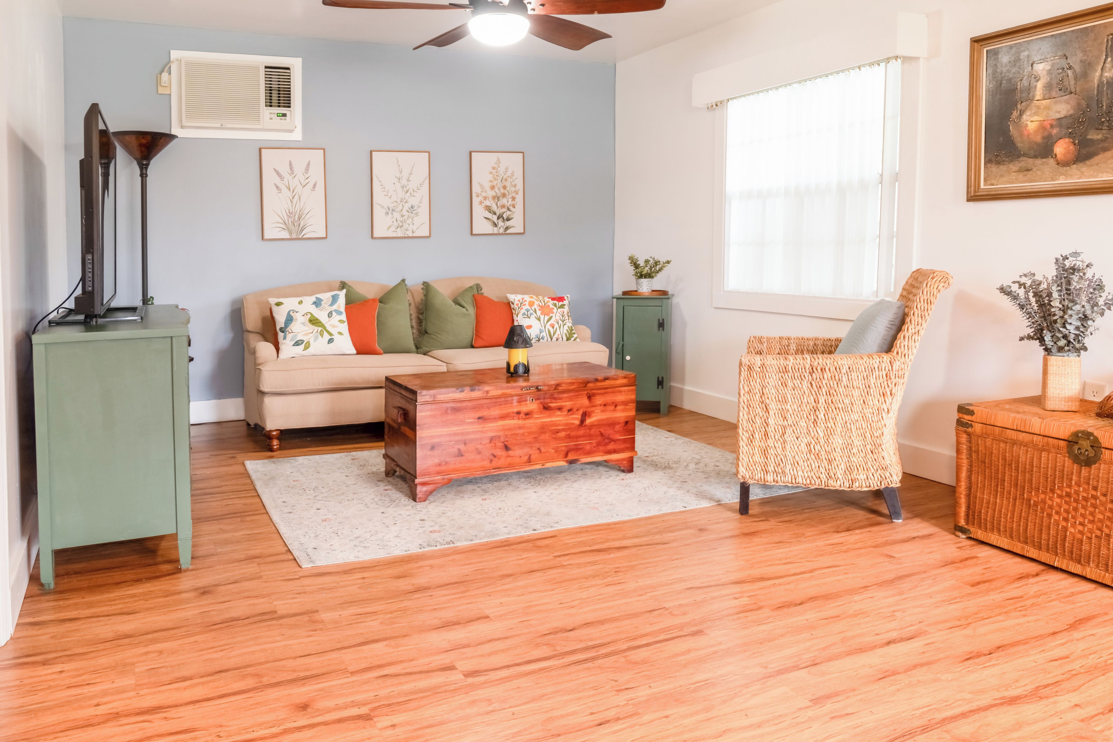 A living room with a sofa, a wooden coffee table, a wicker armchair, a green cabinet, and a painting on the wall.