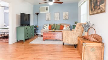 A living room with a sofa, a coffee table, a television, a ceiling fan, and a painting on the wall.
